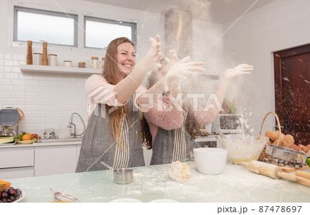 Mom and her younger kids daughter in a modern kitchen area celebrating joyous learning, happy small daughter make prepare sweet pastries with caring mom on weekend at home 87478697