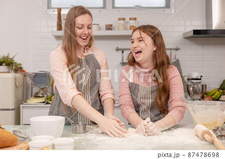 Mom and her younger kids daughter in a modern kitchen area celebrating joyous learning, happy small daughter make prepare sweet pastries with caring mom on weekend at home 87478698
