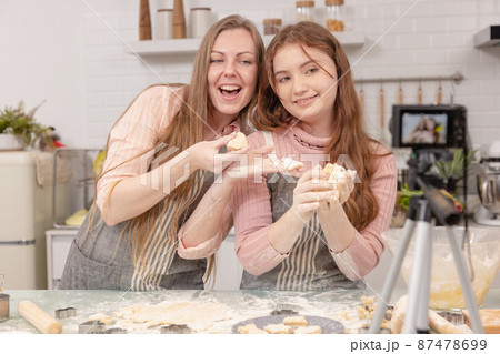 Mom and her younger kids daughter in a modern kitchen area celebrating joyous learning, happy small daughter make prepare sweet pastries with caring mom on weekend at home 87478699