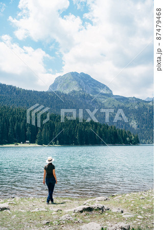 Woman stands on the shore of the bay and looks at the mountains. Back view Woman stands on the shore of the bay and looks at the mountains. Back view 87479468