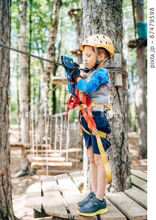 Boy stands on a wooden platform and looks at the safety belt Boy stands on a wooden platform and looks at the safety belt 87479598