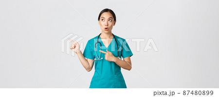 Covid-19, healthcare workers, pandemic concept. Intrigued and amazed beautiful asian female intern, nurse in scrubs or surgeon pointing and looking upper left corner, saying wow in amazement Covid-19, healthcare workers, pandemic concept. Intrigued and amazed beautiful asian female intern, nurse in scrubs or surgeon pointing and looking upper left corner, saying wow in amazement 87480899