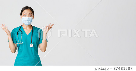 Covid-19, coronavirus disease, healthcare workers concept. Surprised and amazed asian female doctor in medical mask and scrubs, looking impressed, raising hands up, find out good news Covid-19, coronavirus disease, healthcare workers concept. Surprised and amazed asian female doctor in medical mask and scrubs, looking impressed, raising hands up, find out good news 87481587