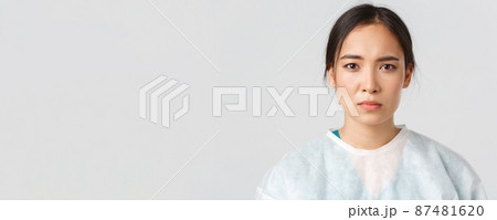 Covid-19, coronavirus disease, healthcare workers concept. Serious exhausted asian female doctor looking tired after shift at hospital, take-off personal protective equipment, have skin marks 87481620