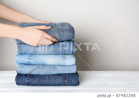 Woman folding stylish jeans on white wooden table, closeup. Space for text 87482268