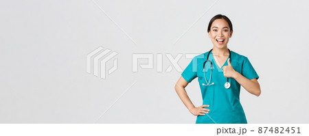 Covid-19, healthcare workers, pandemic concept. Smiling upbeat, confident female asian nurse in scrubs have all under control, show thumbs-up in approval, guarantee quality of service in clinic 87482451
