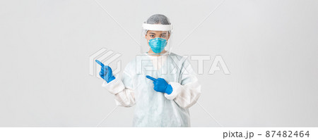 Covid-19, coronavirus disease, healthcare workers concept. Sassy professional asian female doctor, physician or technician in personal protective equipment pointing upper left corner 87482464