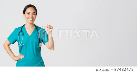 Covid-19, healthcare workers, pandemic concept. Professional confident female asian doctor, nurse in scrubs pointing at herself and smiling, guarantee she knows what do, white background Covid-19, healthcare workers, pandemic concept. Professional confident female asian doctor, nurse in scrubs pointing at herself and smiling, guarantee she knows what do, white background 87482475