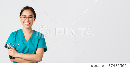 Covid-19, coronavirus disease, healthcare workers concept. Confident happy asian female physician, doctor in glasses, cross arms chest and smiling, holding stethoscope for examination Covid-19, coronavirus disease, healthcare workers concept. Confident happy asian female physician, doctor in glasses, cross arms chest and smiling, holding stethoscope for examination 87482562