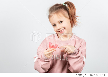 Cute little girl with blond hair is holding a pink dental myofunctional trainer Cute little girl with blond hair is holding a pink dental myofunctional trainer 87483531