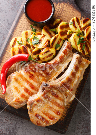 Spicy meat grilled spare Pork Chops and grilled potatoes on a wooden board on the table closeup. Vertical top view Spicy meat grilled spare Pork Chops and grilled potatoes on a wooden board on the table closeup. Vertical top view 87483596