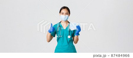 Covid-19, coronavirus disease, healthcare workers concept. Smiling asian doctor, nurse in scrubs and rubber gloves, showing thumbs-up and medical masks, white background Covid-19, coronavirus disease, healthcare workers concept. Smiling asian doctor, nurse in scrubs and rubber gloves, showing thumbs-up and medical masks, white background 87484966