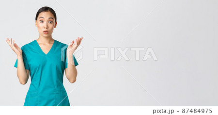Covid-19, healthcare workers, pandemic concept. Surprised and amazed asian nurse in scrubs raising hands up, looking startled, found out big news, hospital got coronavirus vaccine, white background 87484975