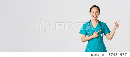 Covid-19, healthcare workers, pandemic concept. Smiling cheerful asian female doctor, therapist in scrubs pointing fingers upper right corner, inviting for checkup, recommend vaccinate Covid-19, healthcare workers, pandemic concept. Smiling cheerful asian female doctor, therapist in scrubs pointing fingers upper right corner, inviting for checkup, recommend vaccinate 87484977