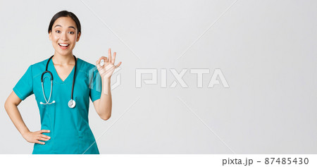Covid-19, healthcare workers, pandemic concept. Surprised and happy asian female doctor, nurse in scrubs showing okay gesture and smiling amazed, praise nice work, agree with someone 87485430