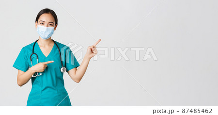 Covid-19, coronavirus disease, healthcare workers concept. Pleasant asian female doctor, medical employee in scrubs and mask, pointing fingers upper right corner, showing advertisement Covid-19, coronavirus disease, healthcare workers concept. Pleasant asian female doctor, medical employee in scrubs and mask, pointing fingers upper right corner, showing advertisement 87485462