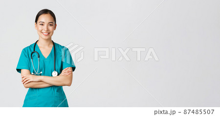 Covid-19, healthcare workers, pandemic concept. Portrait of confident smiling, attractive asian female nurse in scrubs, with stethoscope, cross arms chest and looking at camera, white background 87485507