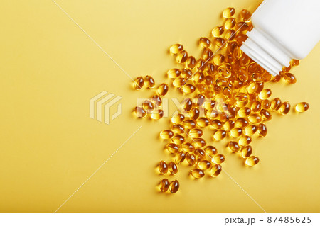 Golden Omega-3 fish oil capsules poured out of a jar on a yellow background Golden Omega-3 fish oil capsules poured out of a jar on a yellow background 87485625