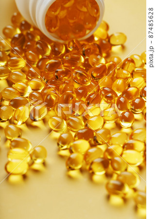 Golden Omega-3 fish oil capsules poured out of a jar on a yellow background 87485628