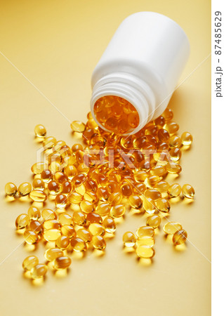 Golden Omega-3 fish oil capsules poured out of a jar on a yellow background 87485629