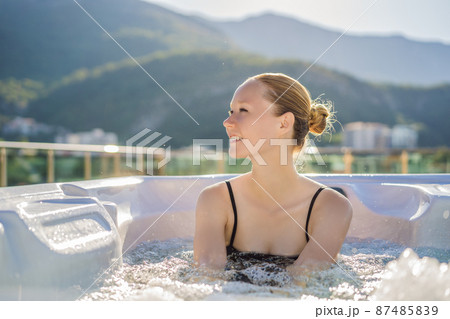 Portrait of young carefree happy smiling woman relaxing at hot tub during enjoying happy traveling moment vacation life against the background of green big mountains Portrait of young carefree happy smiling woman relaxing at hot tub during enjoying happy traveling moment vacation life against the background of green big mountains 87485839
