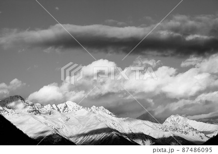 Black and white high snowy winter mountains in sunlight clouds at sunny evening 87486095