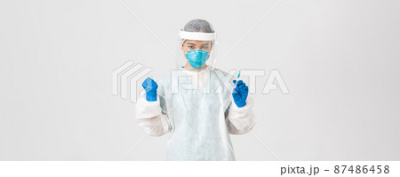 Covid-19, coronavirus disease, healthcare workers concept. Determined and confident female asian doctor, tech lab employee in personal protective equipment holding syringe with vaccine 87486458