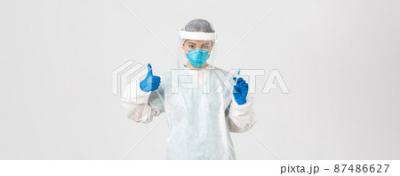 Covid-19, coronavirus disease, healthcare workers concept. Confident serious female asian doctor in personal protective equipment, show thumb-up and hold syringe with vaccine, white background Covid-19, coronavirus disease, healthcare workers concept. Confident serious female asian doctor in personal protective equipment, show thumb-up and hold syringe with vaccine, white background 87486627