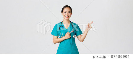 Covid-19, healthcare workers, pandemic concept. Smiling beautiful asian female nurse, intern pointing fingers upper right corner, inviting for checkup, online clinic appointment, white background Covid-19, healthcare workers, pandemic concept. Smiling beautiful asian female nurse, intern pointing fingers upper right corner, inviting for checkup, online clinic appointment, white background 87486904