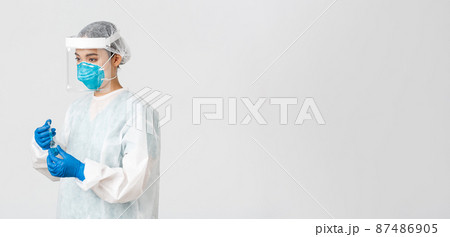 Covid-19, coronavirus disease, healthcare workers concept. Side view of serious young asian female doctor, physician in personal protective equipment insert syringe into ampoule with vaccine 87486905