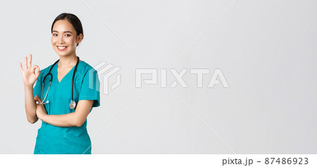 Covid-19, healthcare workers, pandemic concept. Confident professional asian doctor, female physician in scrubs, showing okay gesture, guarantee quality of services in hospital, approve and agree 87486923
