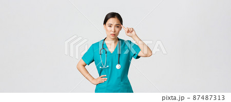 Covid-19, healthcare workers, pandemic concept. Annoyed skeptical asian female nurse or doctor scolding someone acting crazy or stupid, roll finger over temple with judgemental face 87487313