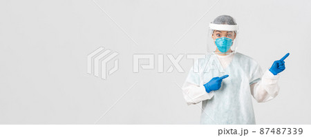 Covid-19, coronavirus disease, healthcare workers concept. Surprised and intrigued asian female doctor, tech lab employee in personal protective equipment look amazed and pointing fingers right 87487339