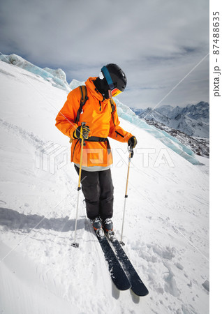 A professional skier athlete in a red jacket, helmet and mask stands on a slope against the backdrop of a glacier and epic mountains. Freeride concept A professional skier athlete in a red jacket, helmet and mask stands on a slope against the backdrop of a glacier and epic mountains. Freeride concept 87488635