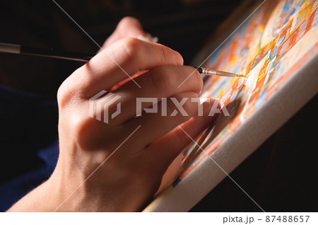 Close-up of a female artist's hand painting with watercolors color on canvas with a brush in a dark modern art studio. The concept of a young artist or female artist. Close-up of a female artist's hand painting with watercolors color on canvas with a brush in a dark modern art studio. The concept of a young artist or female artist. 87488657