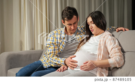 Husband caresses pregnant stomach of wife sitting on sofa Husband caresses pregnant stomach of wife sitting on sofa 87489105