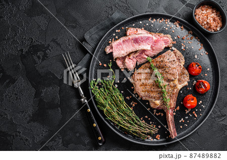 Barbecue sliced rib eye Tomahawk beef veal steak on a plate with pink salt. Black background. Top view. Copy space 87489882
