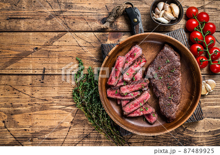 Grilled sliced top blade or denver beef meat steak in a wooden plate with herbs. wooden background. Top view. Copy space 87489925