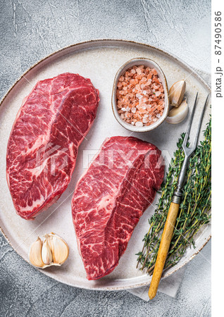 Raw Oyster Top Blade or flat iron roast beef meat steaks on a plate with herbs. White background. Top View Raw Oyster Top Blade or flat iron roast beef meat steaks on a plate with herbs. White background. Top View 87490586