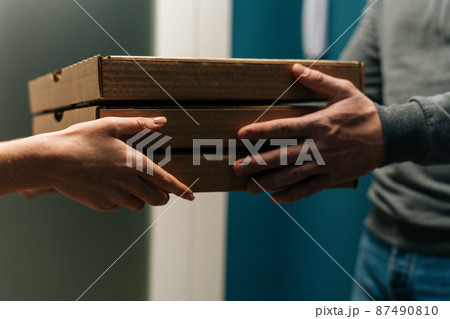 Close-up cropped shot of woman customer receiving carton boxes with takeaway at home from delivery man hands. Closeup side view of courier male delivering to female customer food at home. Close-up cropped shot of woman customer receiving carton boxes with takeaway at home from delivery man hands. Closeup side view of courier male delivering to female customer food at home. 87490810