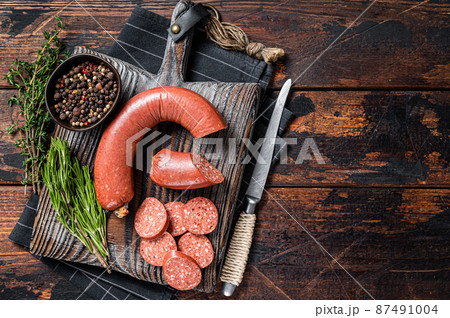 Sliced Sucuk beef meat sausage on a cutting board with herbs. Wooden background. Top view. Copy space 87491004