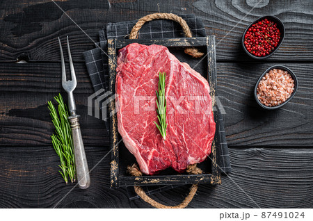 Beef raw fillet for steaks in a wooden tray with herbs. Black wooden background. Top view 87491024