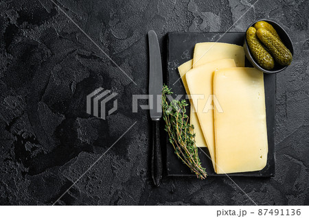 Fresh Uncooked Raclette Swiss cheese slices on marble board. Black background. Top view. Copy space 87491136