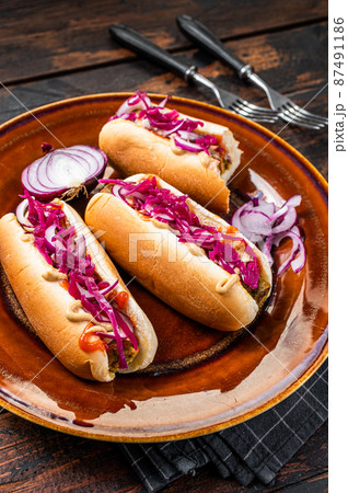Street food - Vegan hot-dogs with cabbage and meatless sausage. Dark Wooden background. Top view Street food - Vegan hot-dogs with cabbage and meatless sausage. Dark Wooden background. Top view 87491186