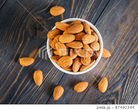 Top view of white bowl with a handful of almond, nuts on a wooden dark background. 87492344