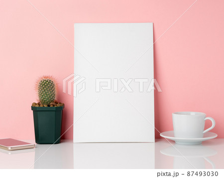 Blank white frame and plant cactus, cup of coffee or tea on a white table against the pink wall with copy space. Mockup with copy space. 87493030
