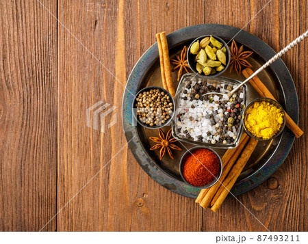 Oriental spice set - coriander, red pepper, turmeric, cinnamon, star anise, various seasonings in metall cups, on brown dark wooden table, top view, macro, empty space. 87493211
