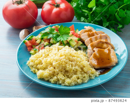 Turkey meat, fried with teriyaki sauce, cucumber salad tomato, vegetables, a side dish of bulgur, side view Turkey meat, fried with teriyaki sauce, cucumber salad tomato, vegetables, a side dish of bulgur, side view 87493624