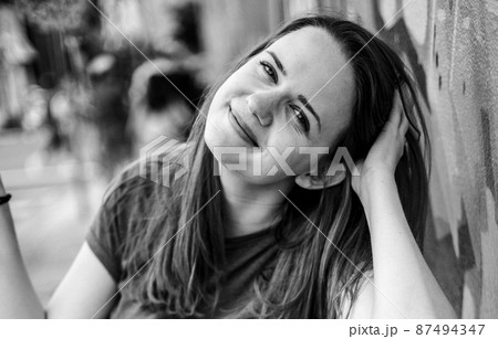 Young and beautiful woman leans against a colorful wall and poses for the camera - typical street Young and beautiful woman leans against a colorful wall and poses for the camera - typical street 87494347