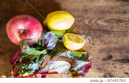 Top view of fresh lemon, apple and beetroot leaves on dark wooden background Top view of fresh lemon, apple and beetroot leaves on dark wooden background 87495763